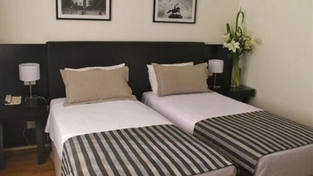 A hotel room with two beds, a nightstand with a lamp, and framed pictures on the wall. - Grand King Hotel (Buenos Aires)