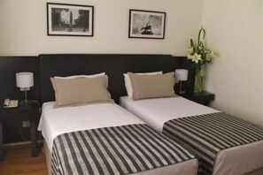 A hotel room with two beds, a nightstand with a lamp, and framed pictures on the wall. - Grand King Hotel (Buenos Aires)