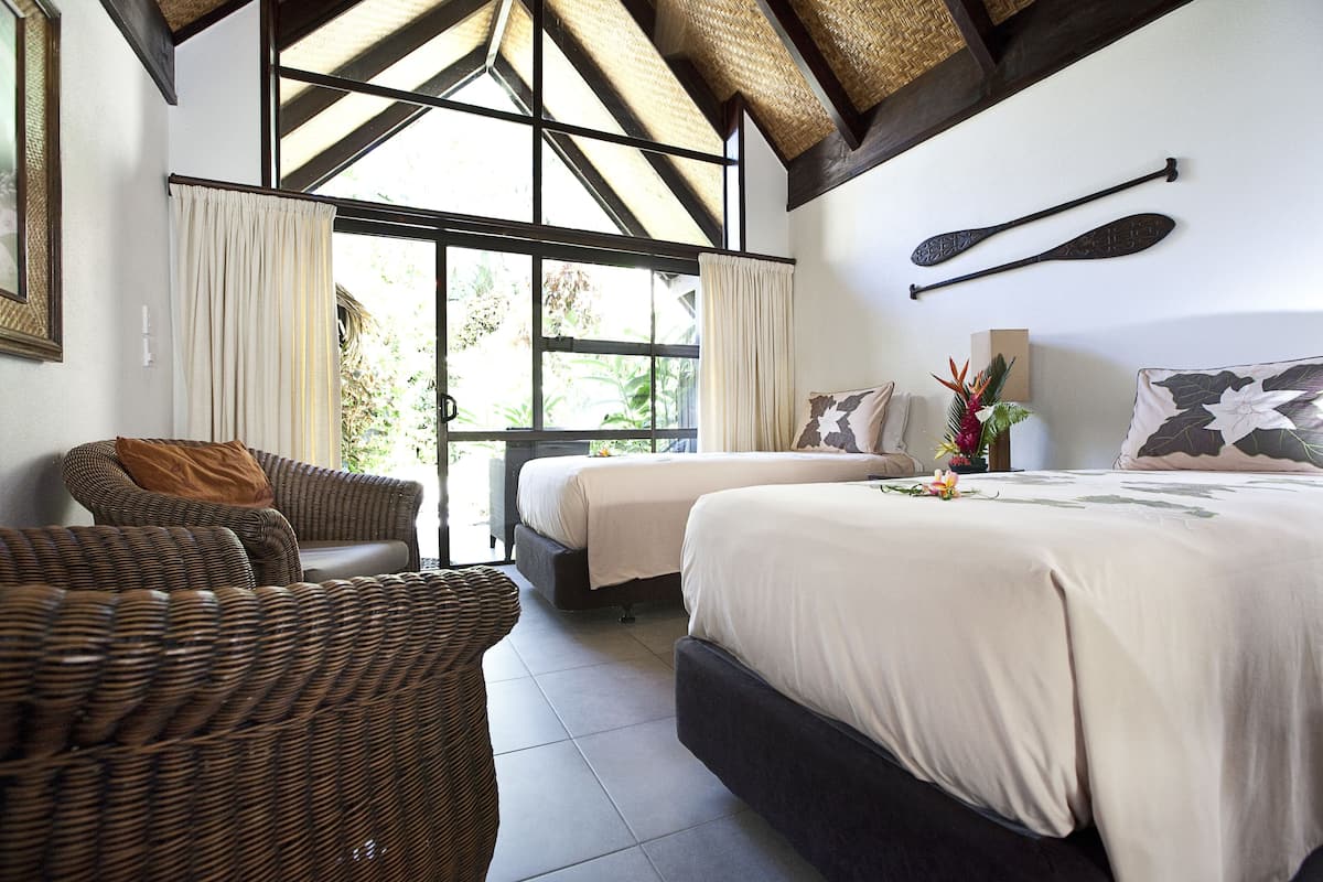 A room with two beds, a wicker sofa, and a large window with curtains.