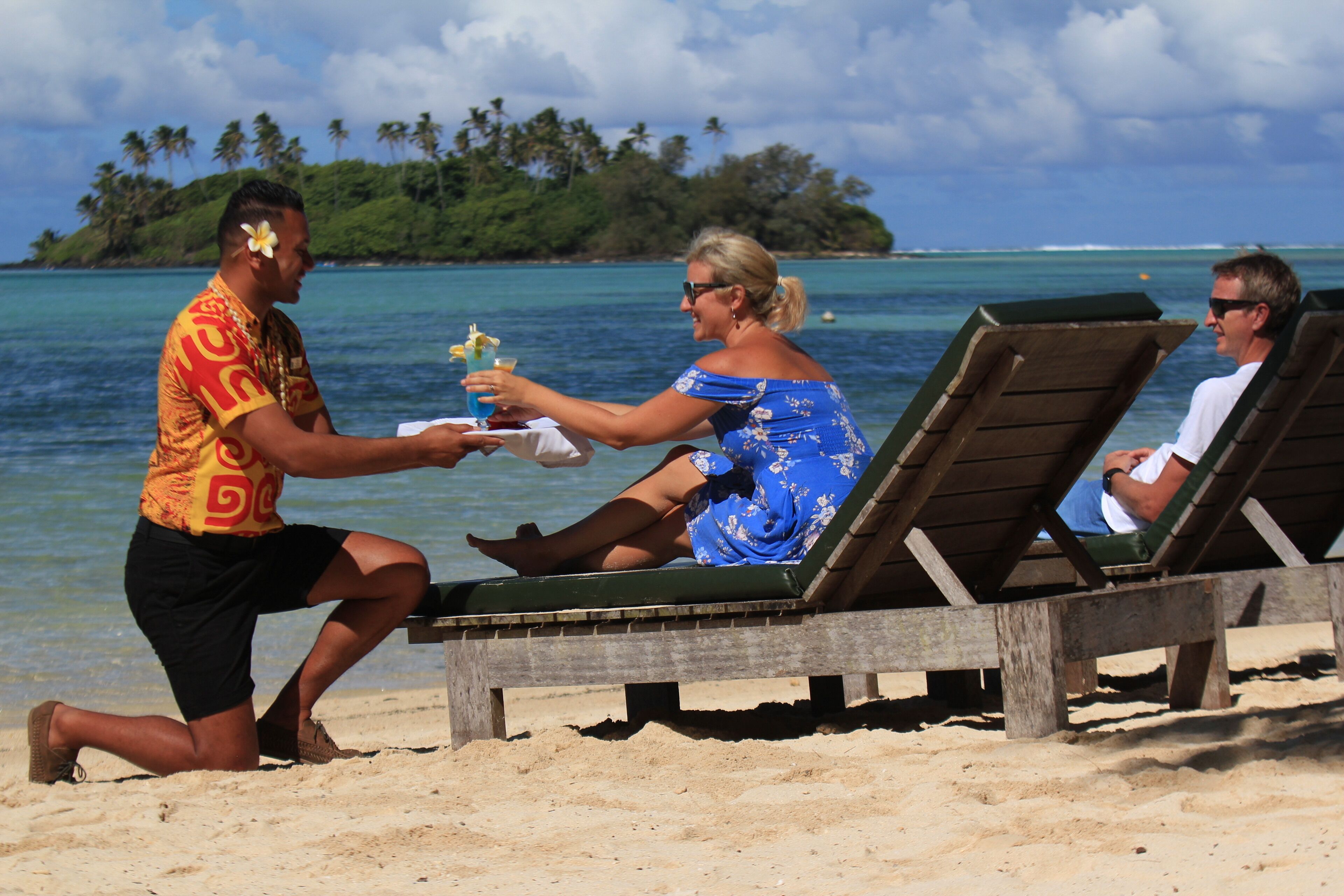 A beach scene with three people, one serving a drink to another.