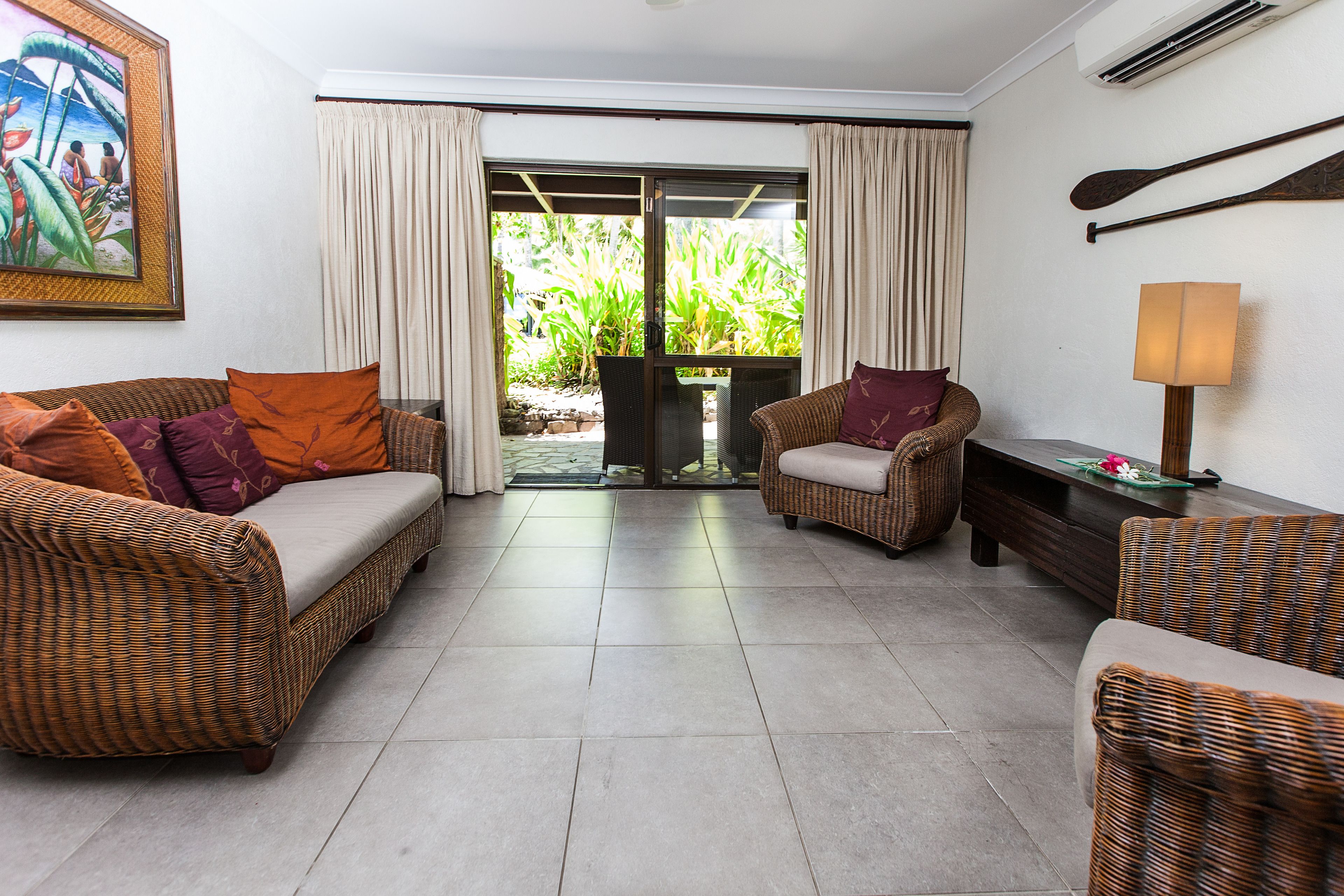 A room with wicker furniture, a large sliding glass door leading to a garden, and a wall-mounted air conditioning unit.