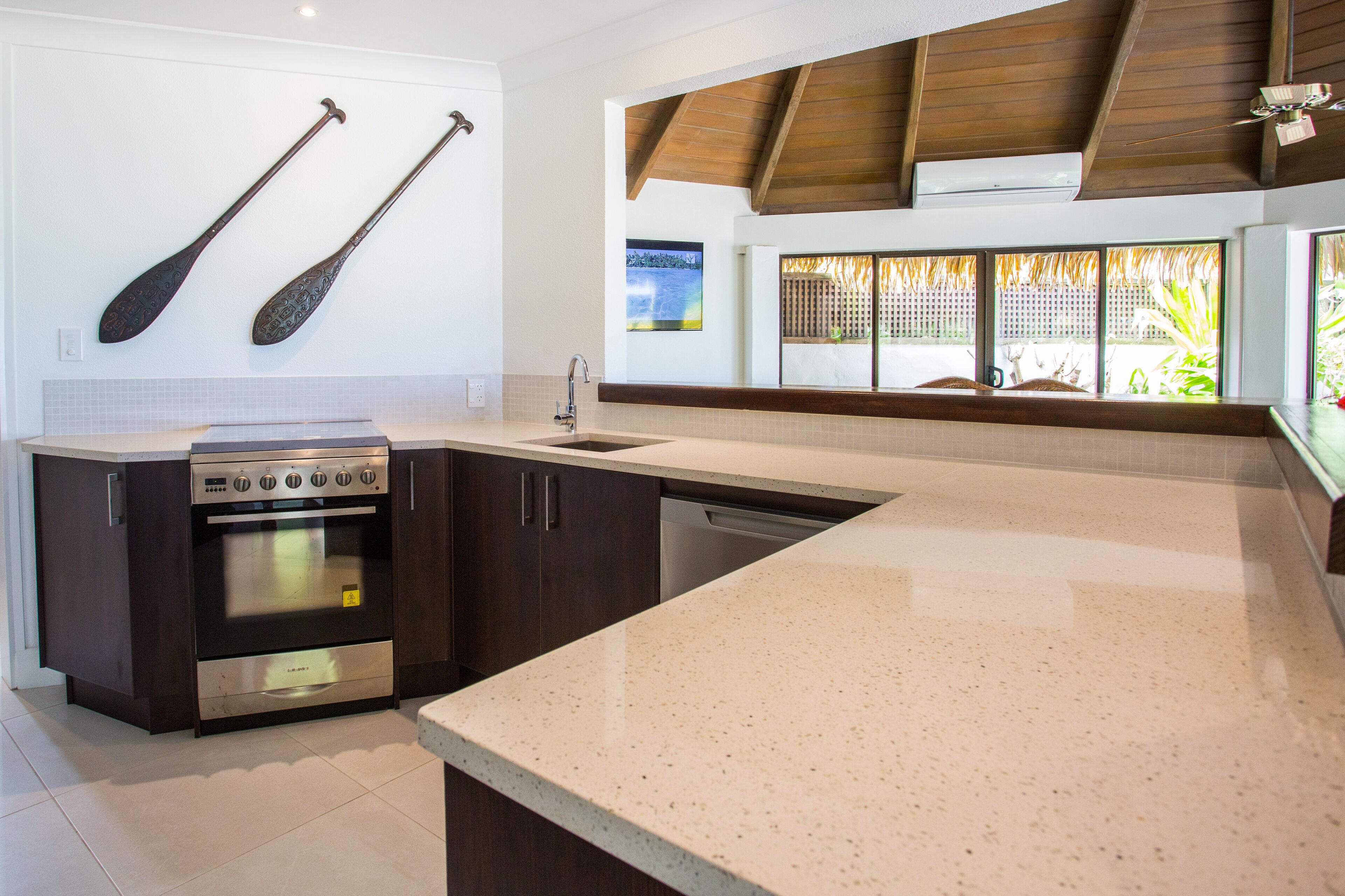 A modern kitchen with dark cabinetry, a stainless steel oven, a dishwasher, and a large island with a speckled countertop.