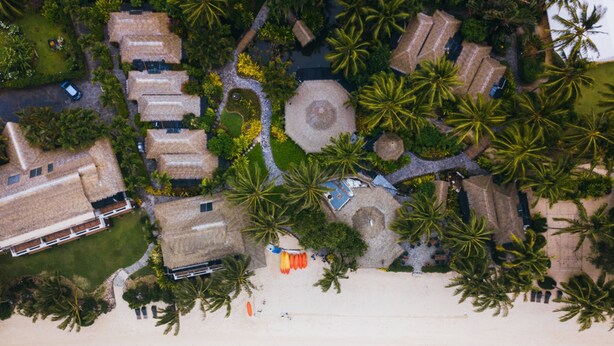 An aerial view of a resort with thatched-roof buildings, palm trees, and a beach. - Pacific Resort Rarotonga (Rarotonga)