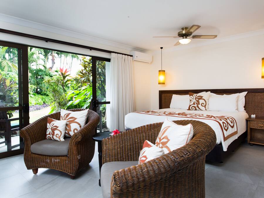 A spacious bedroom with a large bed, two wicker chairs, a small table, and a ceiling fan.