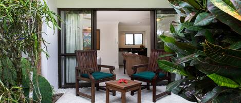 Un patio con una mesa y dos sillas, rodeado de plantas grandes y vistas al interior.