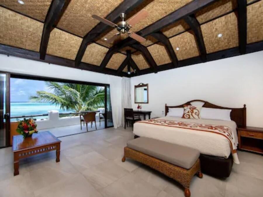 A bedroom with a large bed, a desk, a chair, and a view of the ocean.