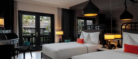 Habitación de hotel con dos camas, un escritorio y una silla. Hay cortinas, una lámpara y vistas al exterior.