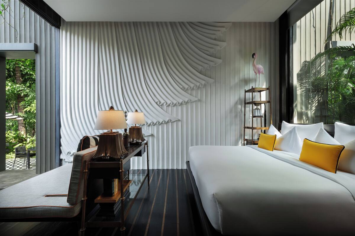 A modern hotel room with a large bed, bedside tables, and a view of greenery.
