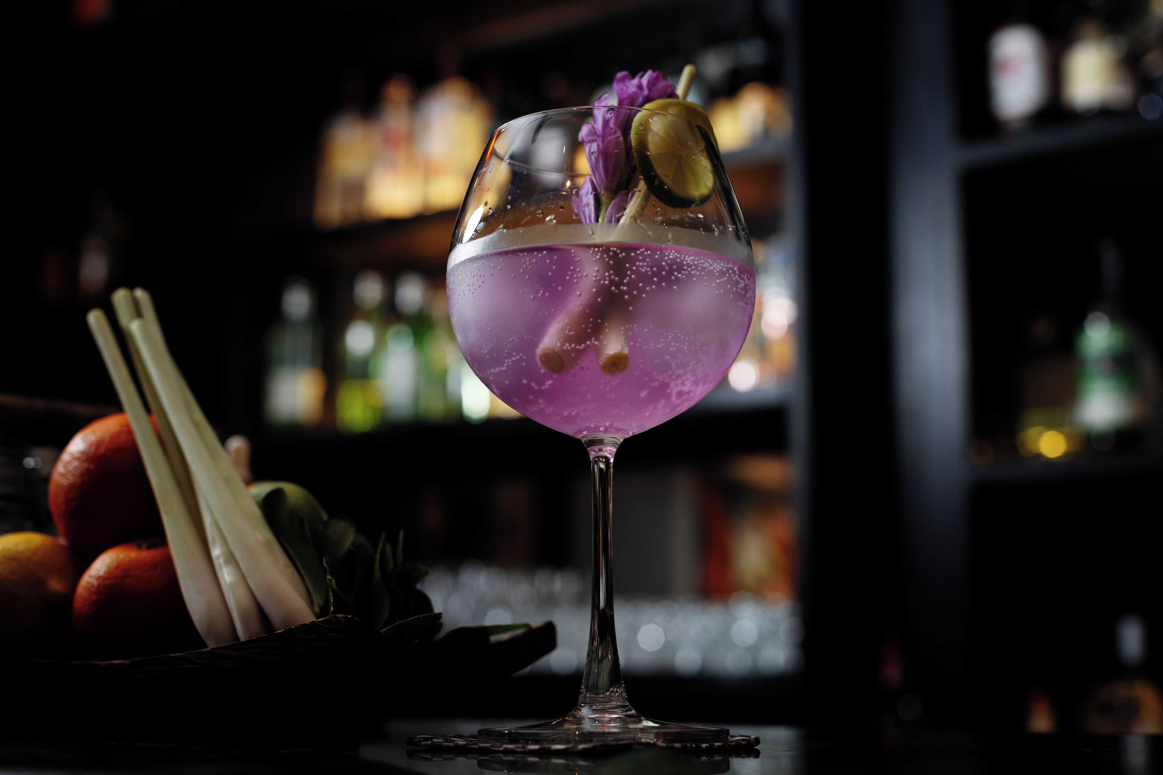 A cocktail glass with a purple drink, garnished with a flower and a slice of lime, placed on a coaster.