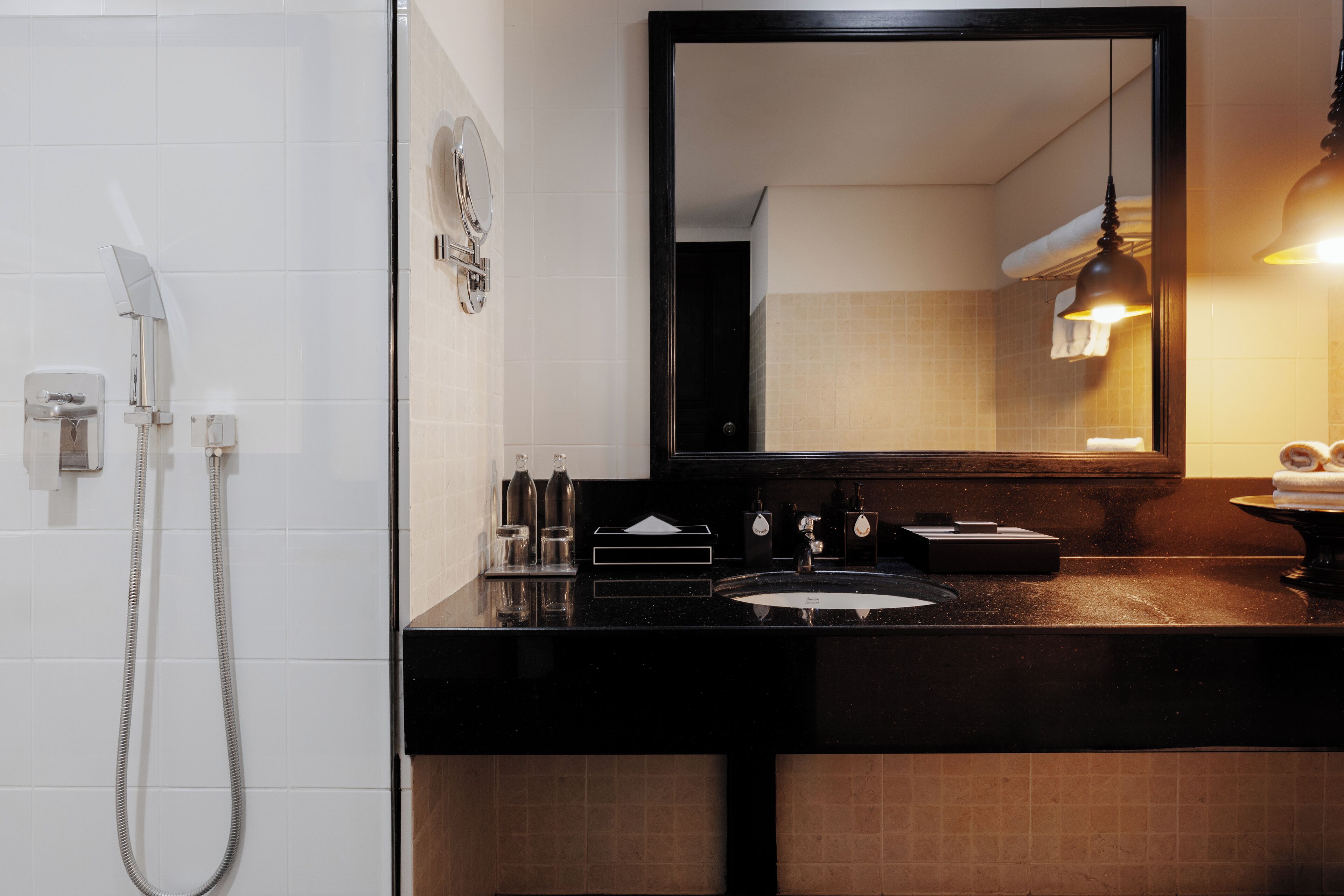 Un baño con encimera negra, lavabo, espejo y ducha.