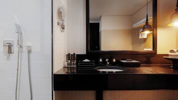 Un baño con encimera negra, lavabo, espejo y ducha.