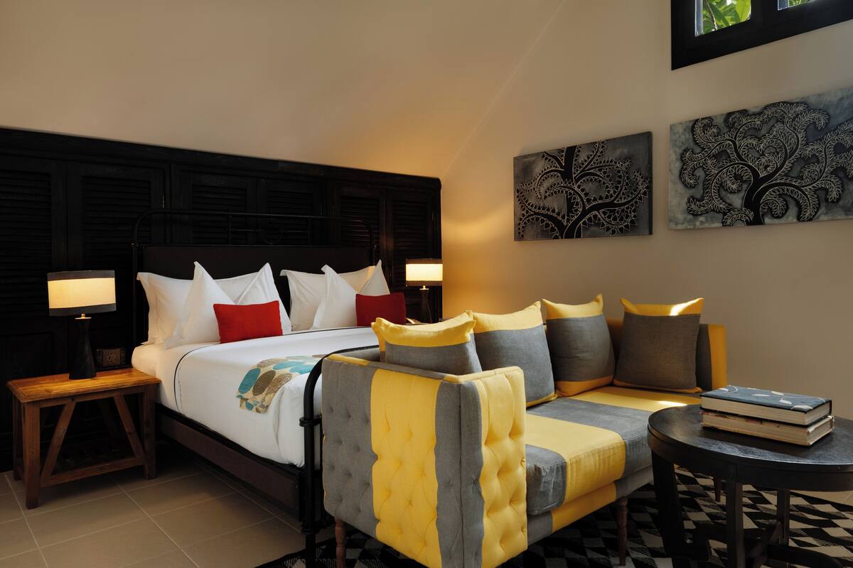 A hotel room with a bed, a sofa, a nightstand, and two wall art pieces.