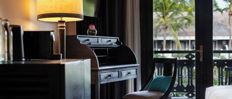 A hotel room with a desk, a chair, a bed, a TV, and a balcony with a view of palm trees.
