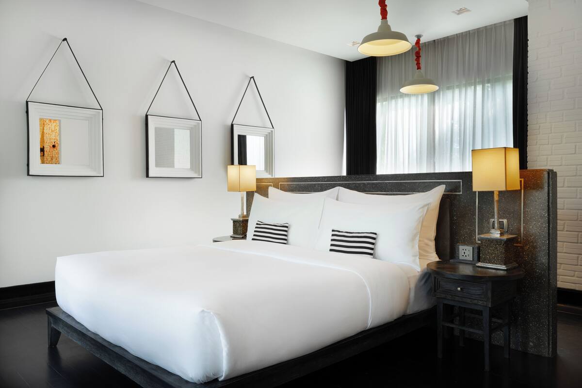 A modern hotel room with a large bed, two bedside tables, a nightstand, and a window with curtains.