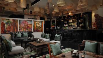 Uma área de bar com disposição de assentos, incluindo um sofá e cadeiras, e um balcão com garrafas e copos.