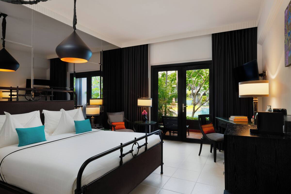 A hotel room with a large bed, a desk, and a view of greenery outside.