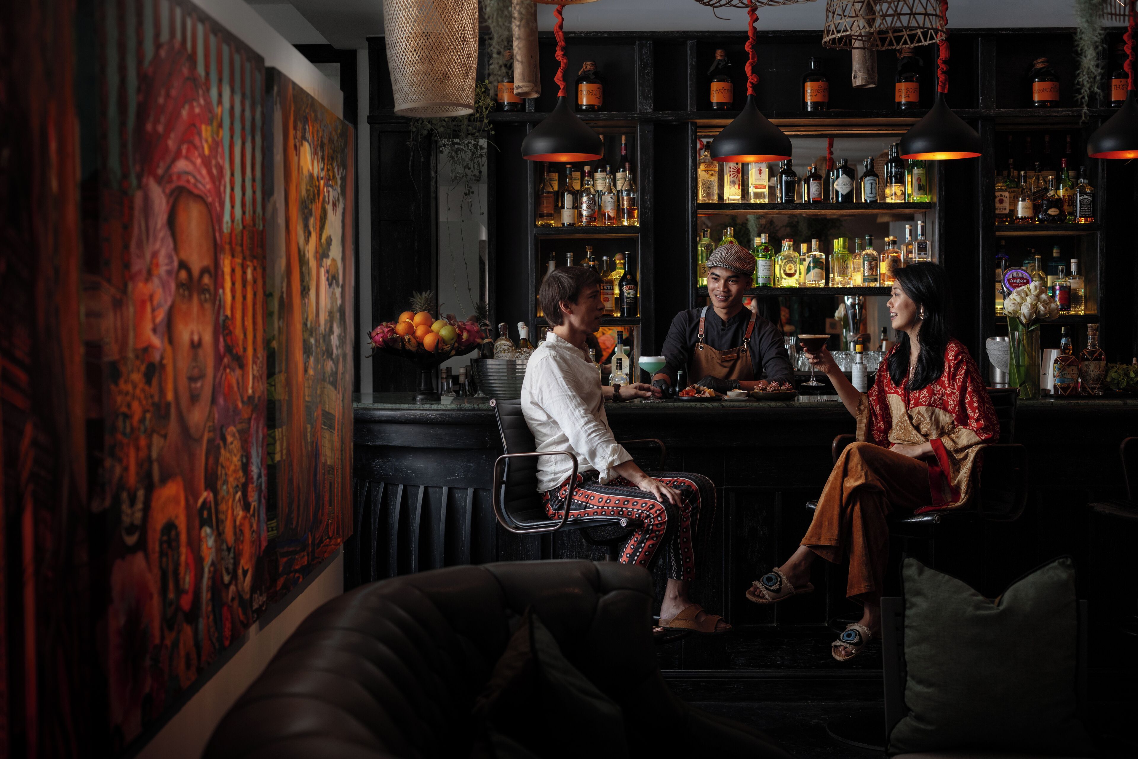 A bar area with a large mural, shelves with bottles, and a seating area with a couch and chairs.