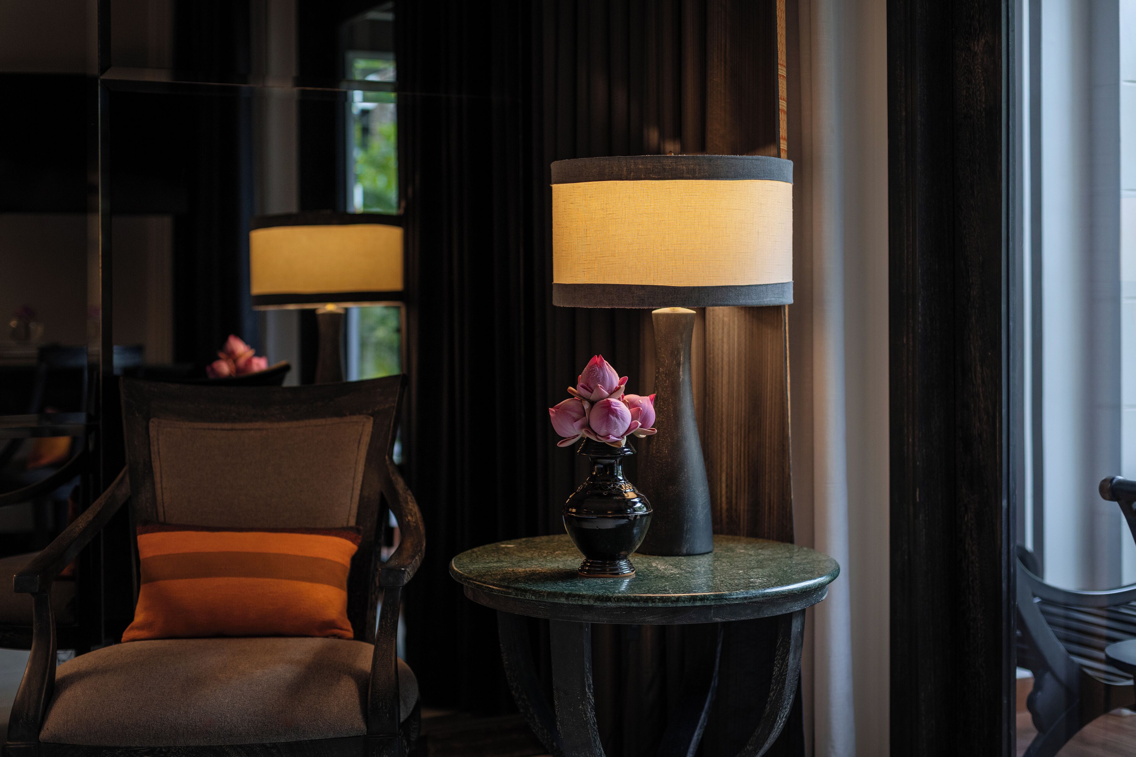 A room with a chair, a table with a lamp, and a vase with flowers.