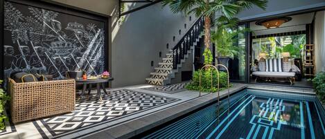 Un espace piscine extérieur moderne, agrémenté d'un motif géométrique en carreaux, d'un canapé en osier, d'un escalier et d'un coin salon avec un canapé et des lampes.