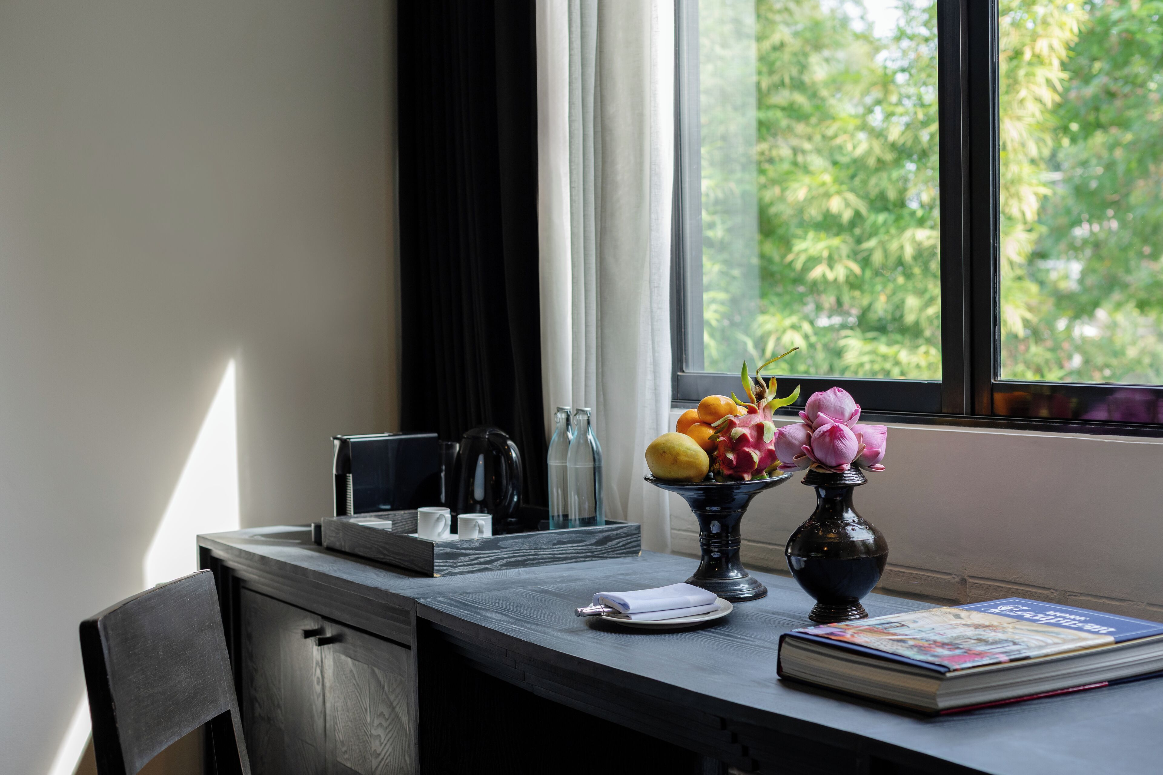 A table with a book, a vase with flowers, and a fruit bowl.
