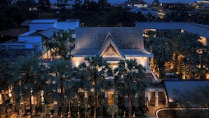 A modern hotel with a triangular roof, surrounded by palm trees and a swimming pool.