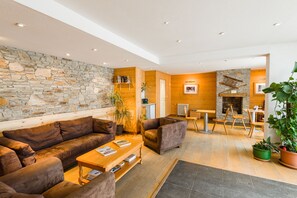 A modern living room with a stone wall, wooden paneling, a fireplace, and comfortable seating. - Résidence Lagrange Vacances Les Pics d'Aran (Bagneres-de-Luchon)