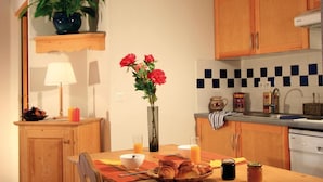 Eine Küche mit Holzausstattung, gefliestem Spritzschutz, einer Blumenvase, einem Frühstückstisch mit Croissants und einer Kaffeemaschine.