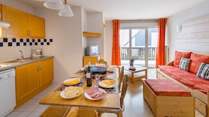 Eine kompakte Küche mit Holzschränken, einem Essplatz für eine Mahlzeit, einer Couch und einem Fernseher.