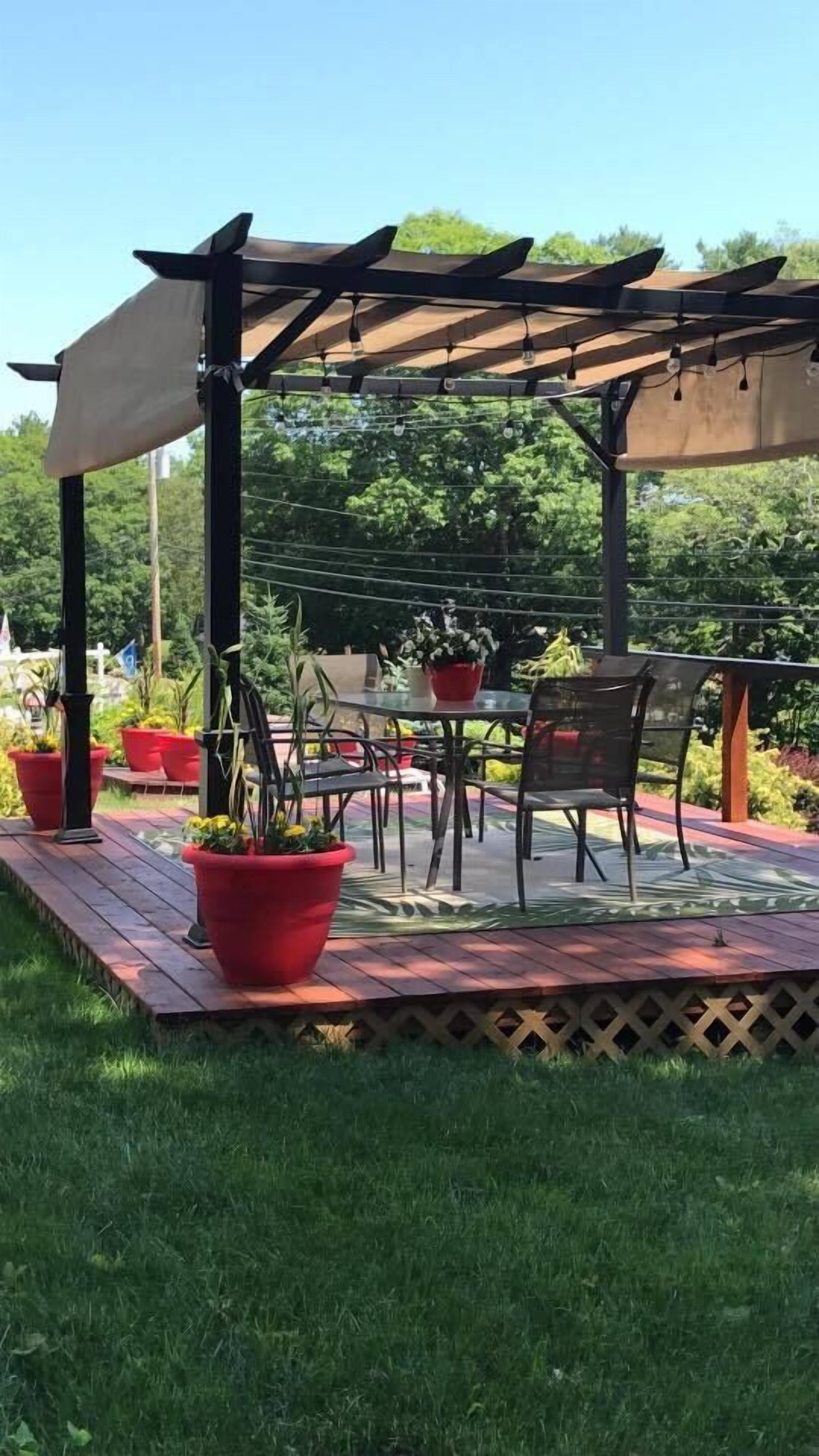An outdoor patio with a pergola, a table, chairs, and potted plants.