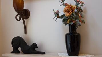 A black cat sculpture on a shelf, a vase with a rose, and a wall-mounted light fixture.