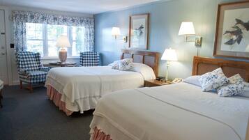 A hotel room with two beds, a checkered chair, a lamp, and a painting on the wall.