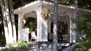 A covered outdoor seating area with steps leading up to it, surrounded by trees and plants. - Mount Battie Inn (Lincolnville)