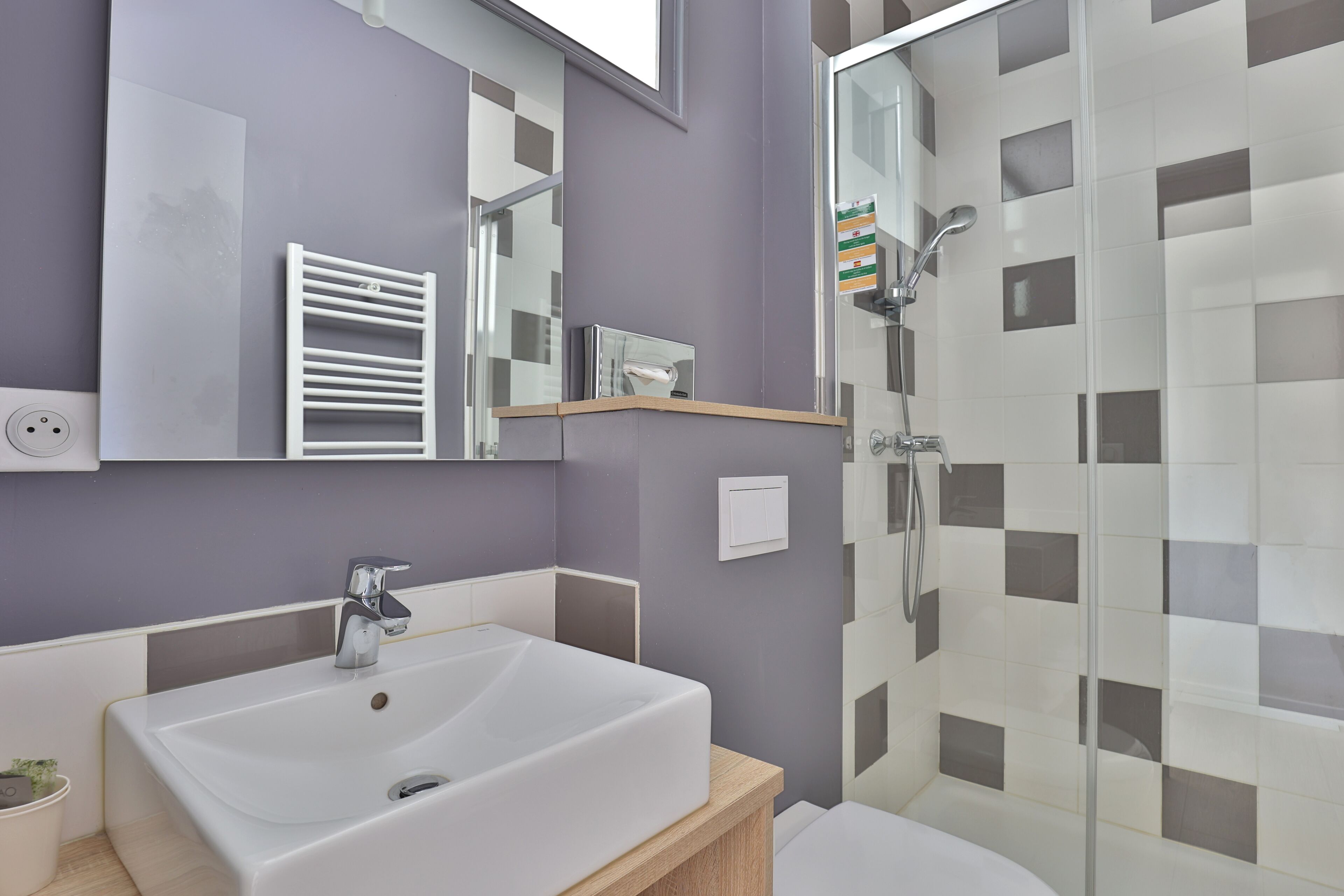 A bathroom with a white sink, a mirror, a towel rack, and a shower enclosure.