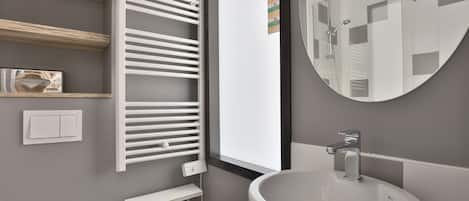 Un baño moderno con un espejo grande, un lavabo redondo, un perchero para toallas y una ventana.