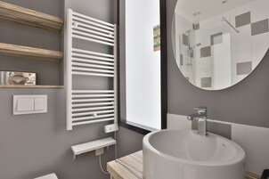 Un baño moderno con un espejo grande, un lavabo redondo, un perchero para toallas y una ventana.