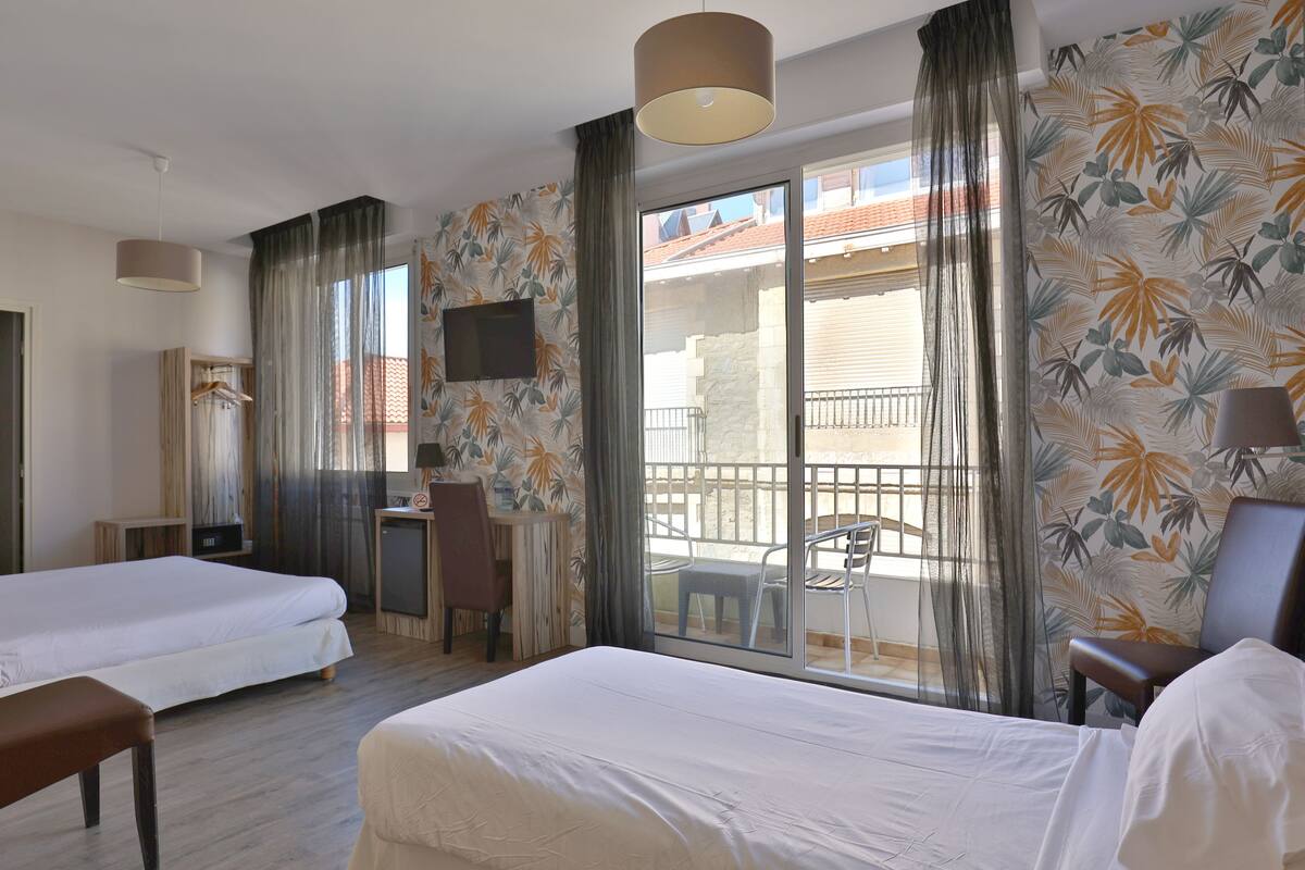 A hotel room with two beds, a desk, a chair, and a balcony with a view.