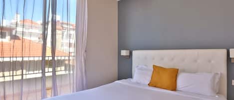 A hotel room with a large bed, a grey accent wall, and a view through sheer curtains.