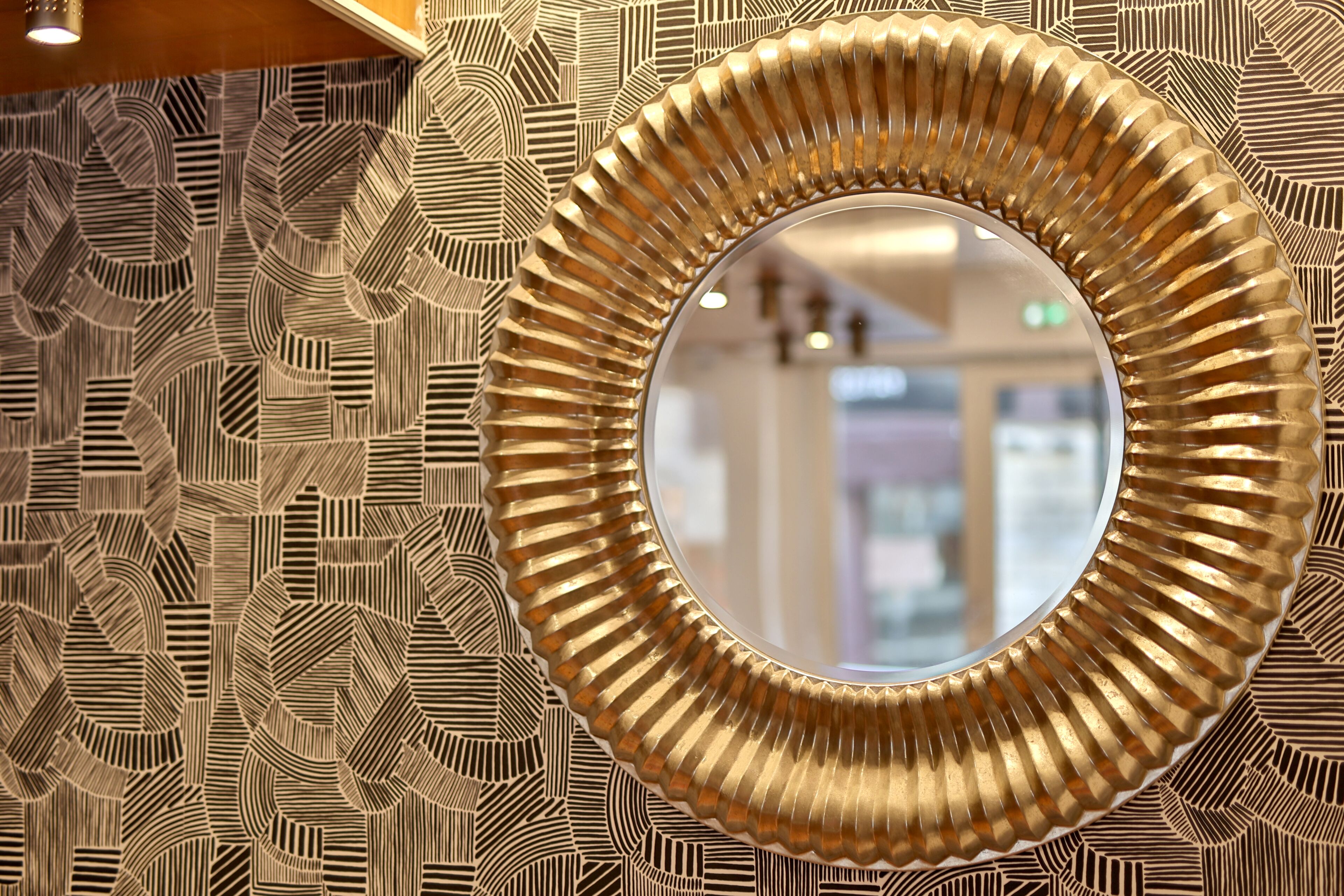 A wall with a geometric patterned wallpaper and a circular mirror with a ribbed frame.