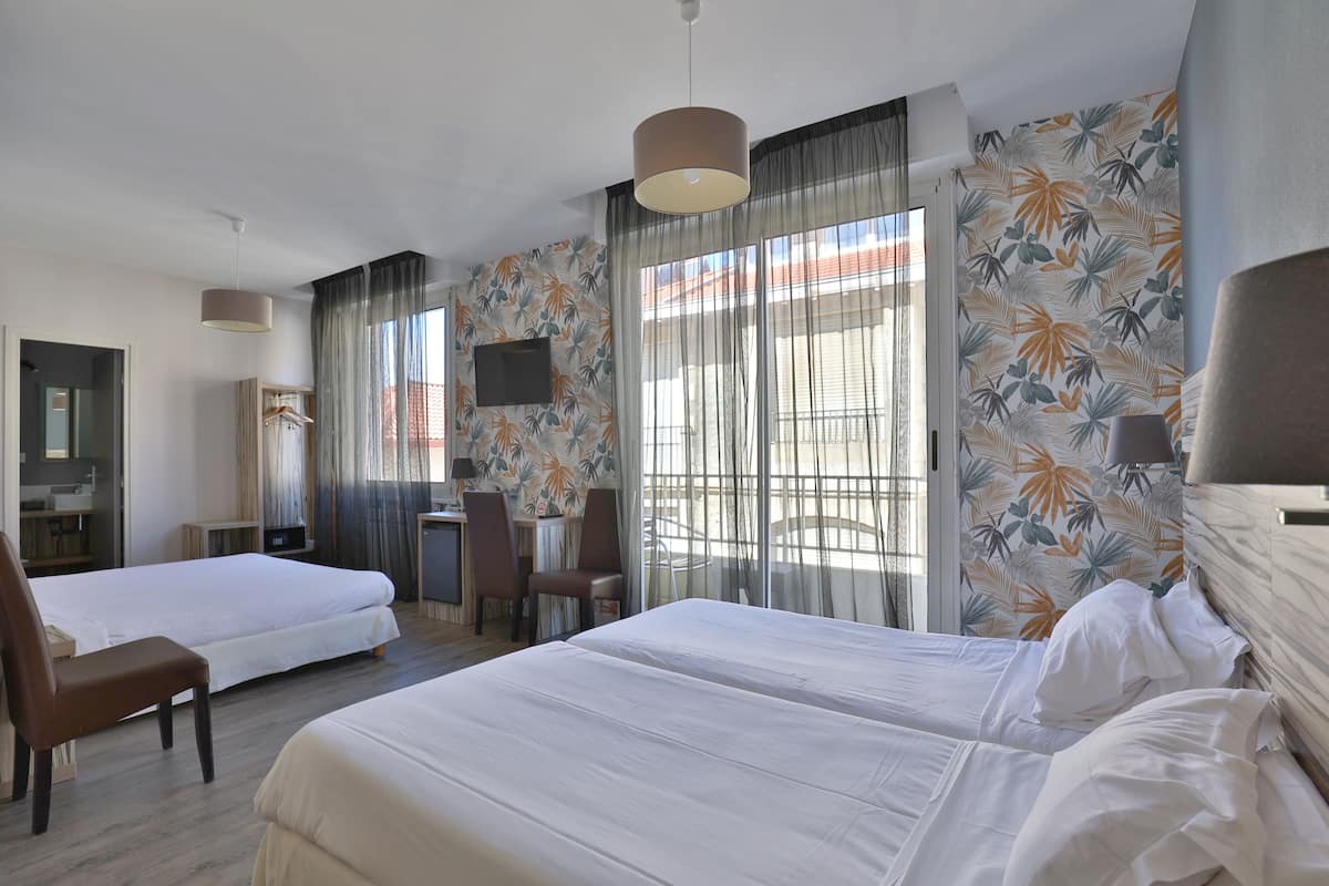 A hotel room with two beds, a desk, a chair, and a TV.