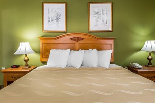 Habitación de hotel con una cama, dos mesitas de noche, una mesita auxiliar, un cabecero de madera y dos cuadros enmarcados en la pared.