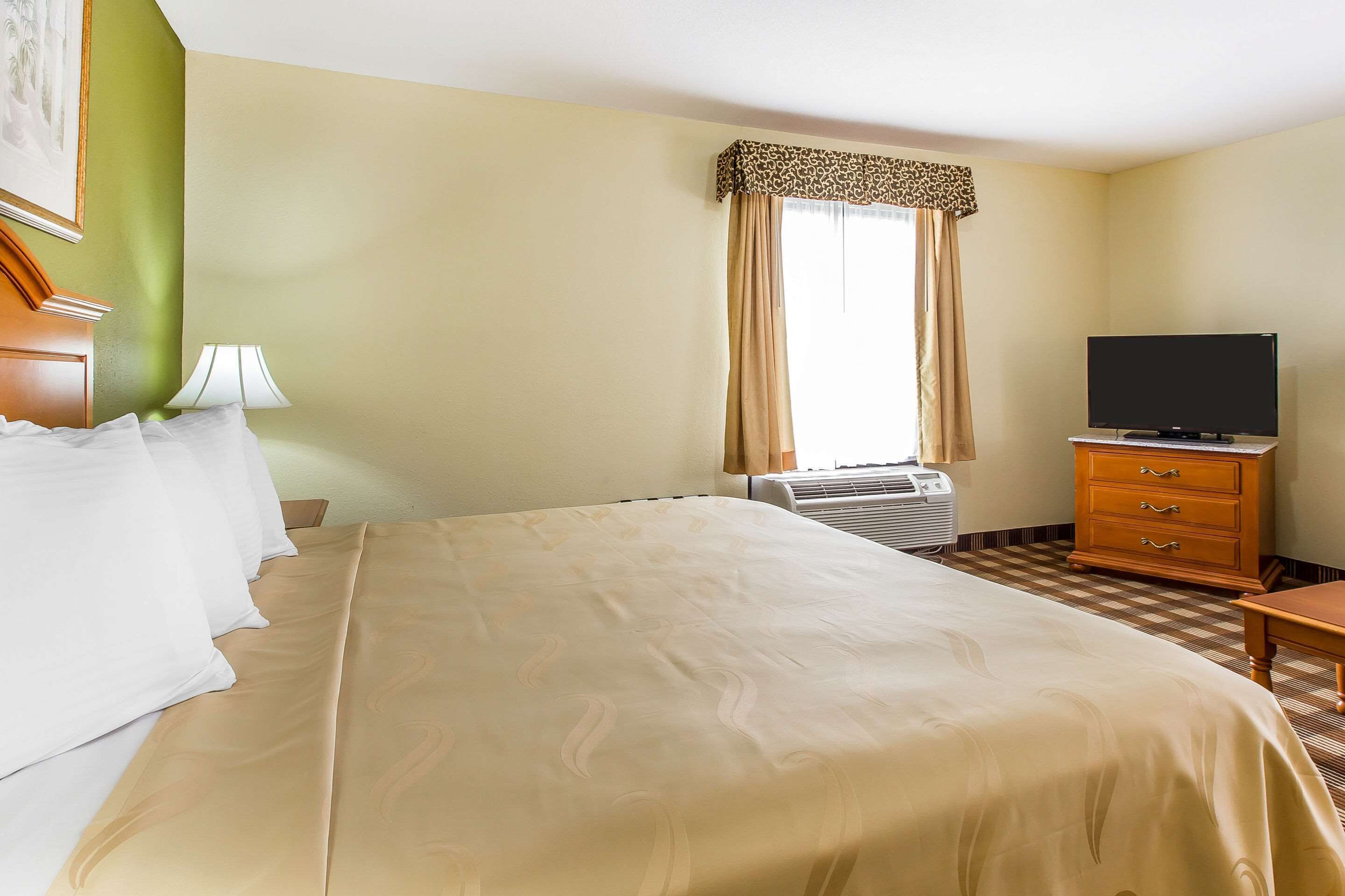Habitación de hotel con cama, televisión, cómoda y ventana con cortinas.