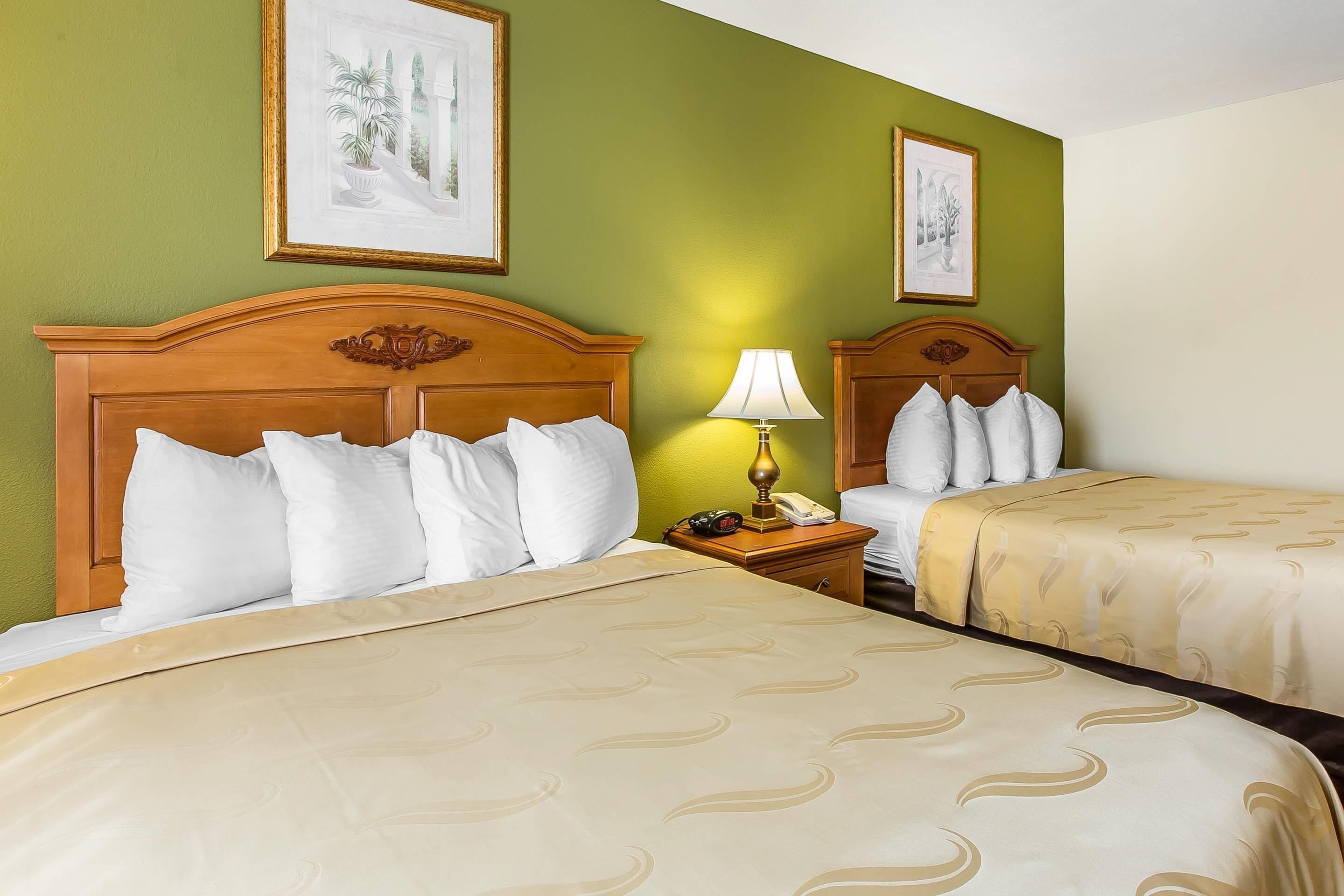 Une chambre d’hôtel avec deux lits, une table de chevet avec une lampe et des œuvres d’art encadrées accrochées aux murs.