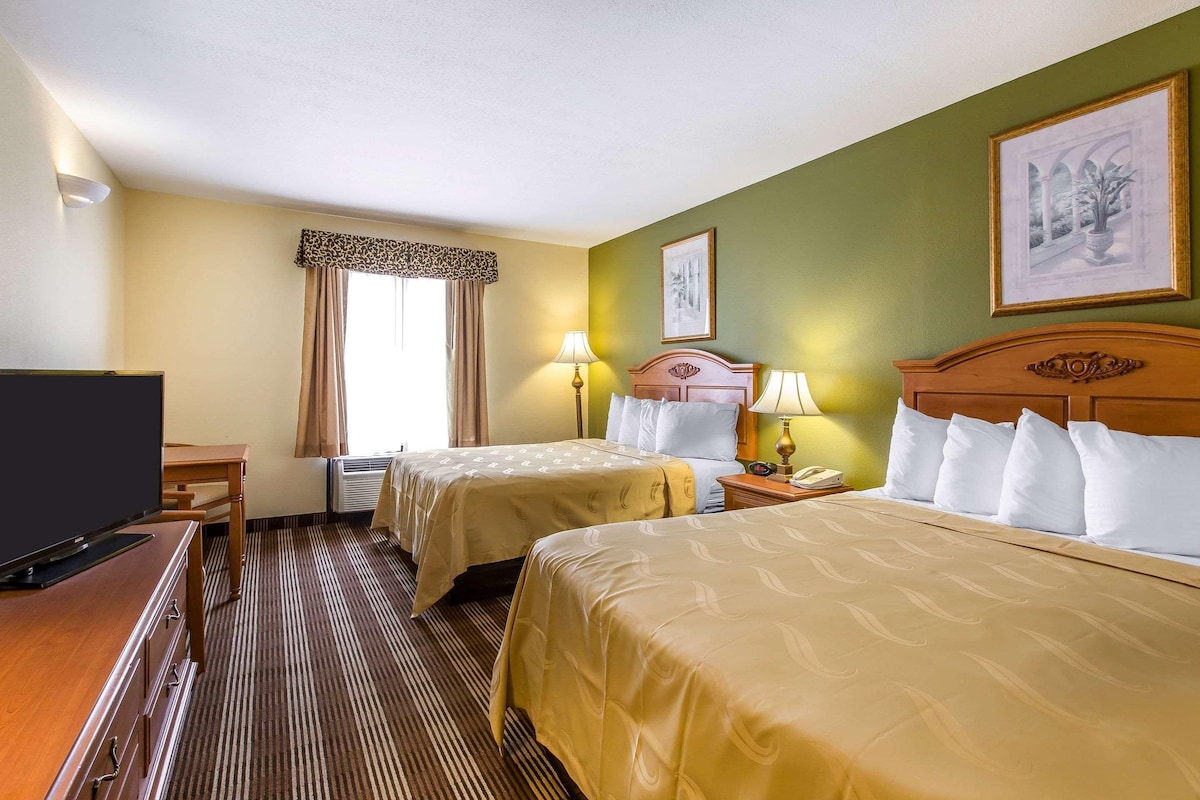 Habitación de hotel con dos camas, televisión, escritorio y ventana con cortinas.