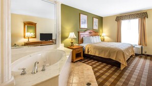 A hotel room with a large bathtub, a bed with a headboard, two bedside lamps, and a window with curtains.