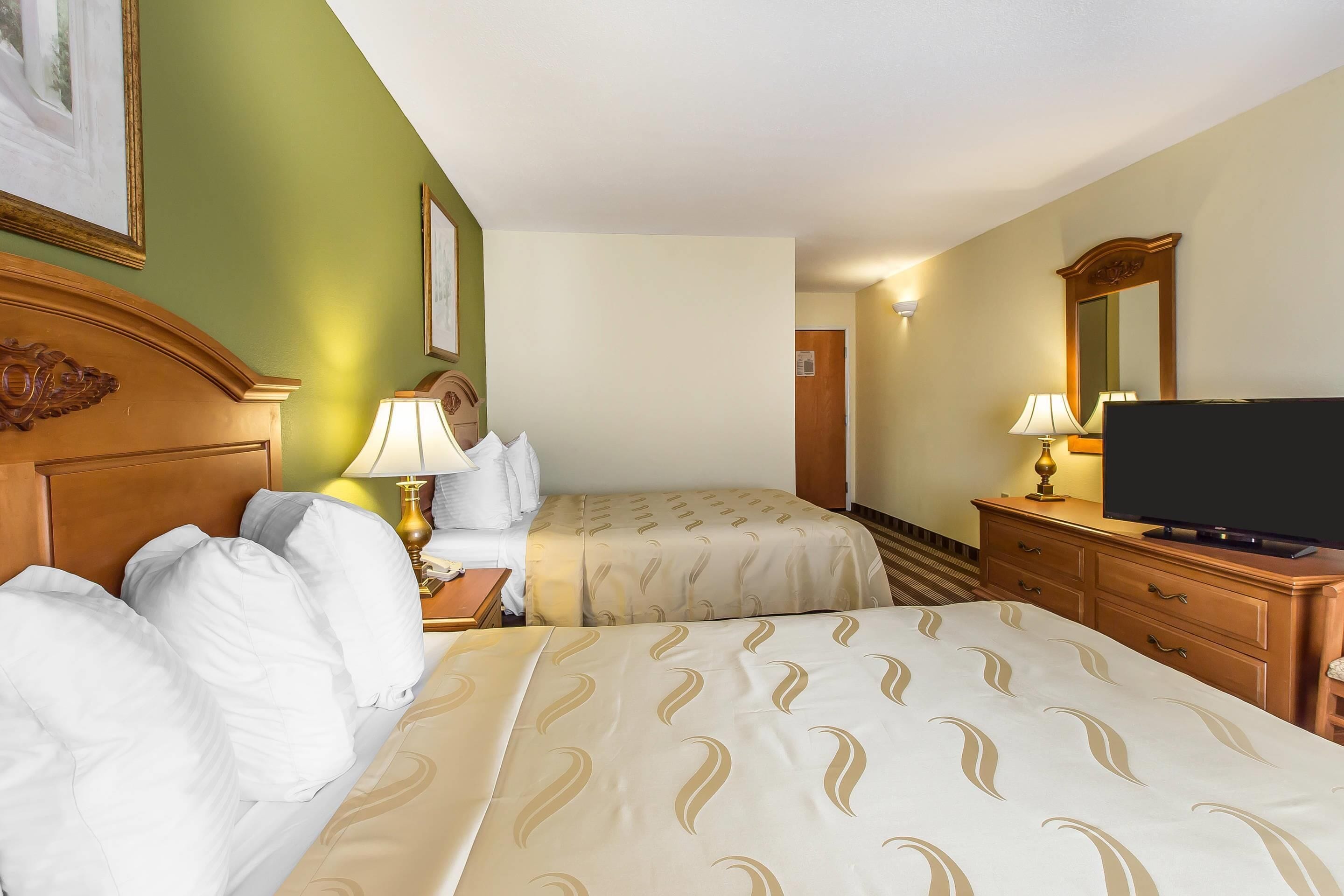 A hotel room with two beds, a television, a dresser, and a mirror.