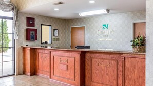 A reception desk with a wooden finish, a digital display, and a sign for Quality Inn by Choice Hotels.