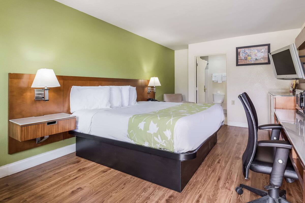 Een hotelkamer met een bed, nachtkastjes, een bureau met stoel, een televisie en een badkamer die door een open deur zichtbaar is.