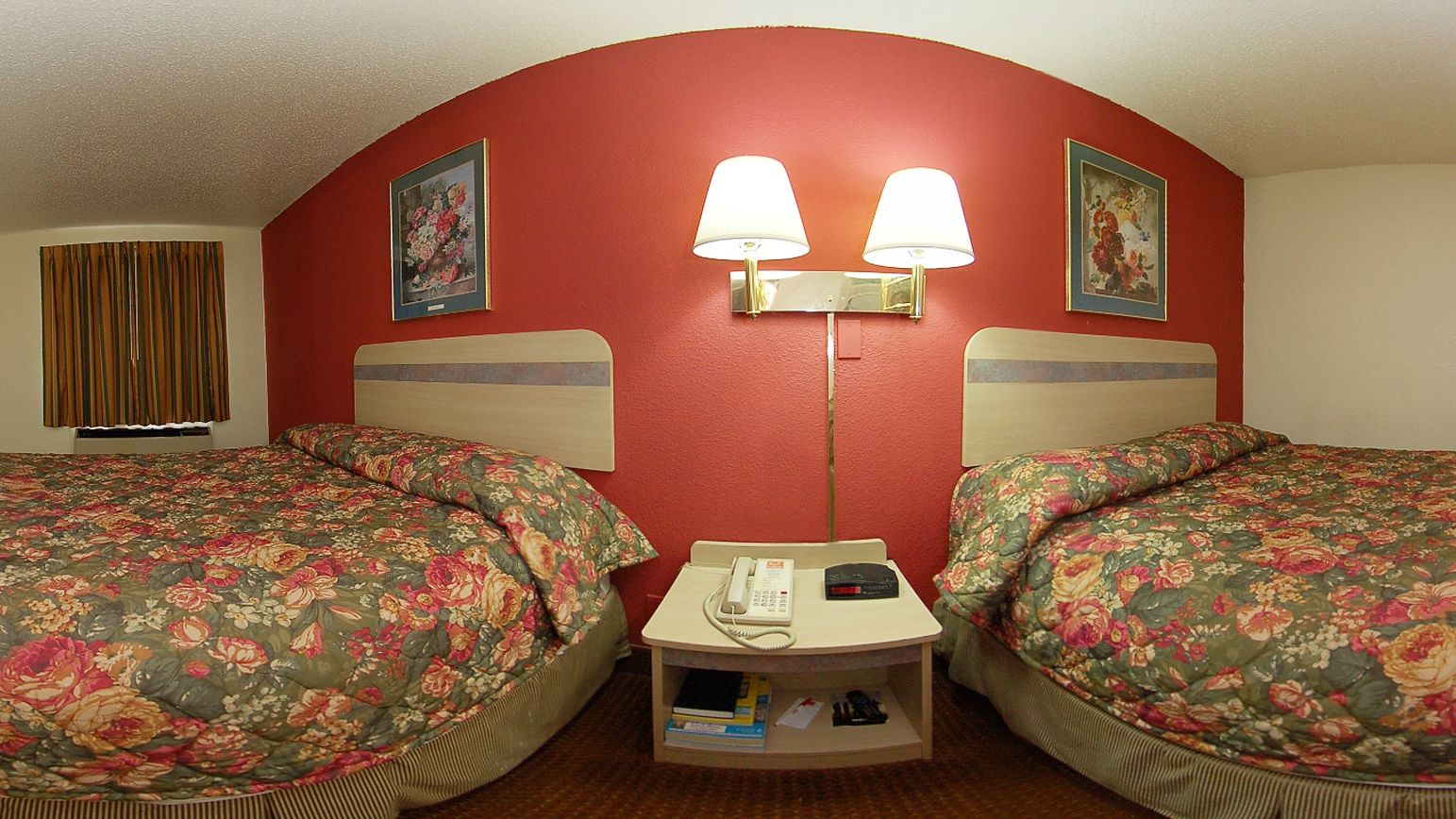Habitación de hotel con dos camas, cada una con ropa de cama floral, una mesita de noche con lámpara y teléfono.