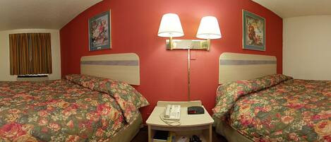 Habitación de hotel con dos camas, cada una con ropa de cama floral, una mesita de noche con lámpara y teléfono.