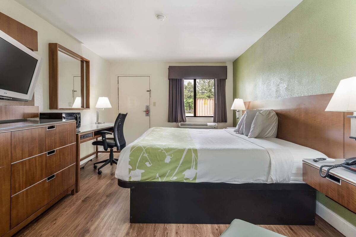 Hotelkamer met een bed, bureau, stoel, televisie en een raam met gordijnen.